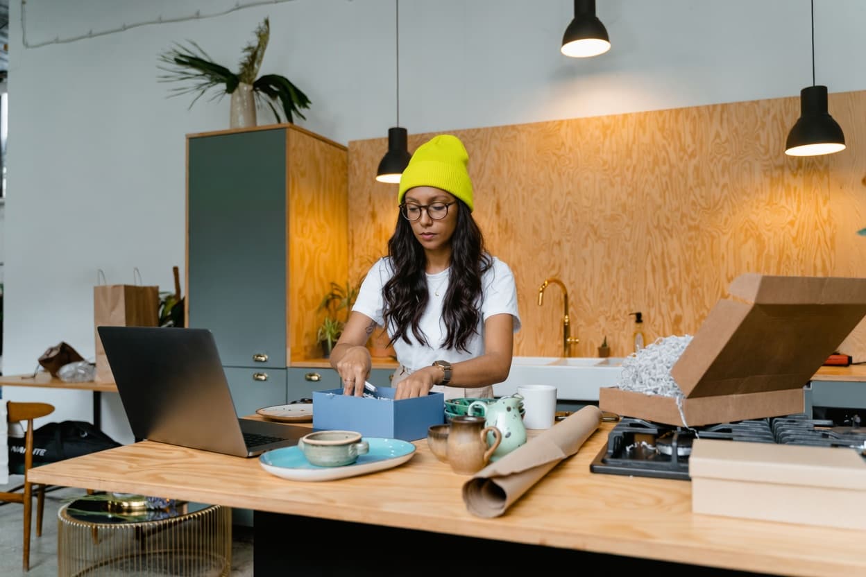 Entrepreneur packing orders at her workshop with a laptop
